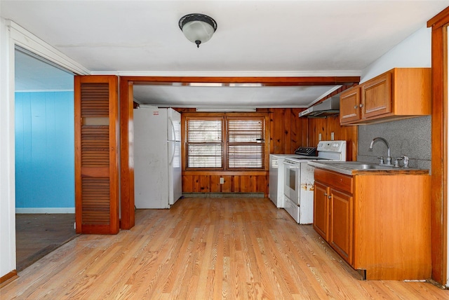 kitchen with sink, white appliances, decorative backsplash, light wood-type flooring, and wood walls