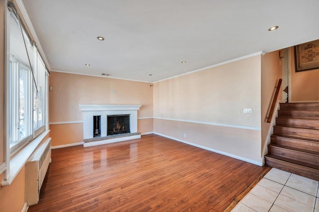 unfurnished living room with a brick fireplace, ornamental molding, and light hardwood / wood-style floors