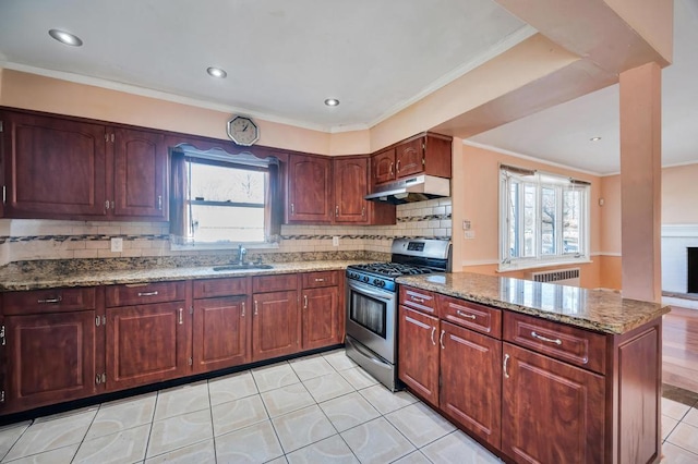 kitchen with radiator, a wealth of natural light, sink, dark stone counters, and gas range