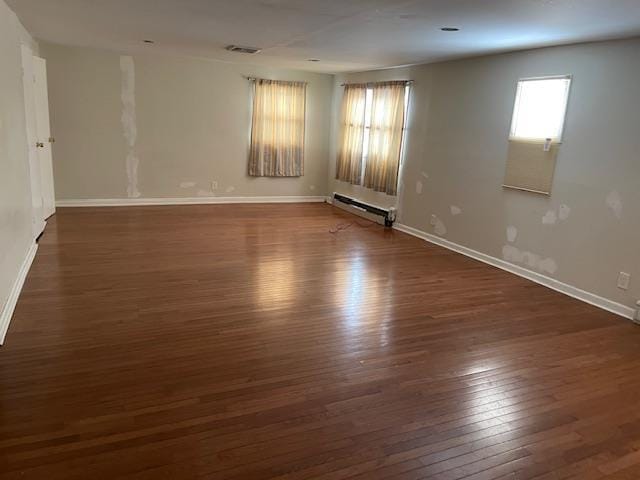 unfurnished room with dark wood-type flooring, plenty of natural light, and baseboard heating