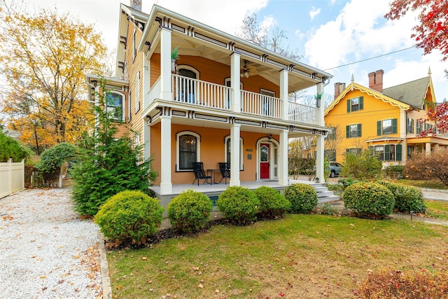 view of front of property with ceiling fan, a porch, a balcony, and a front lawn