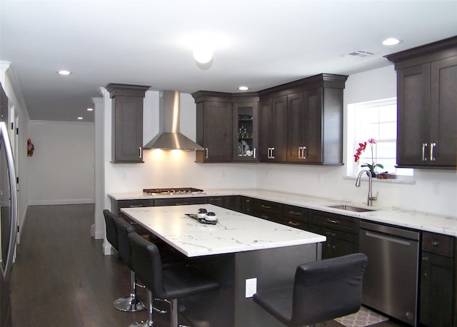 kitchen with wall chimney range hood, sink, appliances with stainless steel finishes, a kitchen breakfast bar, and a kitchen island