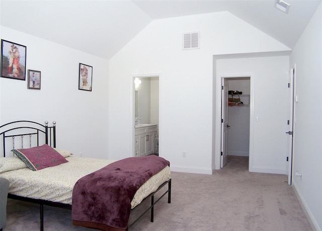 bedroom with vaulted ceiling, a walk in closet, light colored carpet, and ensuite bath