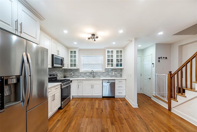 kitchen with sink, light hardwood / wood-style flooring, appliances with stainless steel finishes, decorative backsplash, and white cabinets