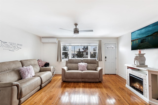 living room featuring ceiling fan, a stone fireplace, light hardwood / wood-style floors, and an AC wall unit