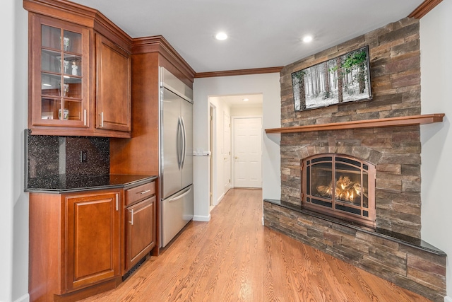 kitchen with built in refrigerator, a fireplace, light wood-type flooring, tasteful backsplash, and glass insert cabinets