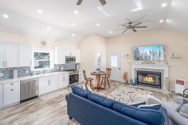 living room with vaulted ceiling, ceiling fan, and light wood-style floors