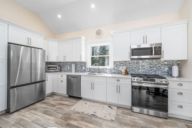 kitchen featuring stainless steel appliances, lofted ceiling, light countertops, white cabinetry, and a sink