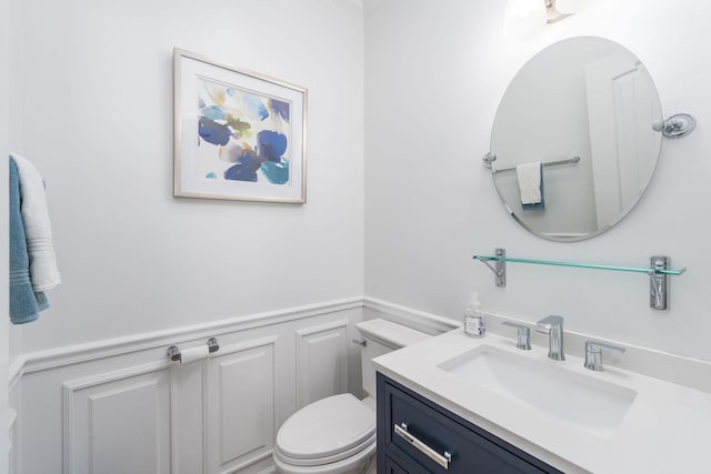 half bathroom featuring toilet, vanity, a decorative wall, and wainscoting