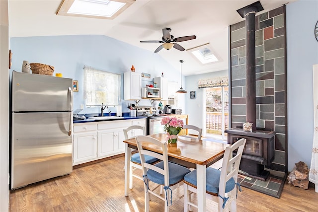 dining room with sink, a wood stove, ceiling fan, vaulted ceiling with skylight, and light wood-type flooring