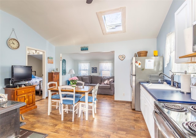 kitchen with lofted ceiling with skylight, sink, white cabinetry, light wood-type flooring, and stainless steel appliances