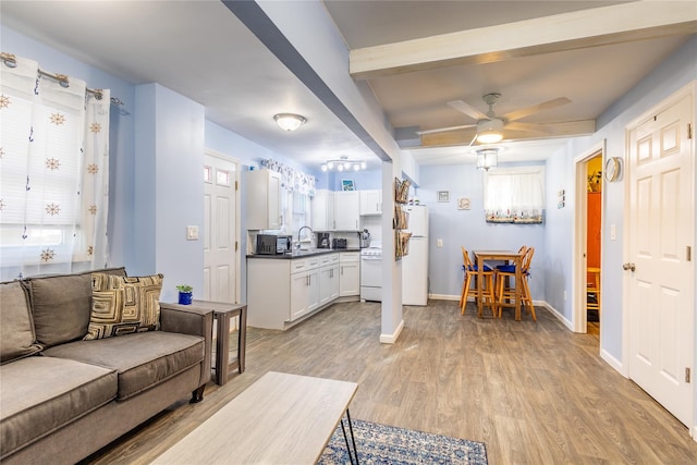 living room featuring sink, light wood-type flooring, plenty of natural light, beamed ceiling, and ceiling fan