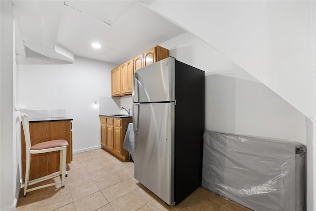 kitchen with stainless steel fridge, sink, light brown cabinets, and light tile patterned floors