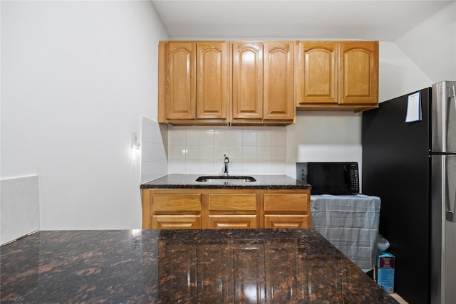 kitchen with stainless steel refrigerator, sink, decorative backsplash, and dark stone countertops