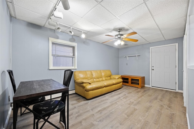 living room with a paneled ceiling, rail lighting, a baseboard radiator, ceiling fan, and light wood-type flooring