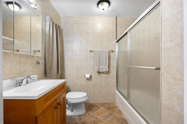 full bathroom featuring tile patterned floors, toilet, shower / bath combination with glass door, tile walls, and vanity