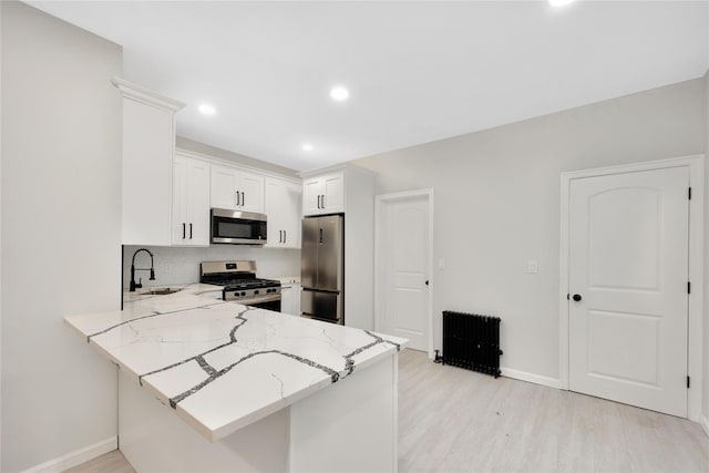 kitchen with radiator, sink, appliances with stainless steel finishes, white cabinetry, and kitchen peninsula