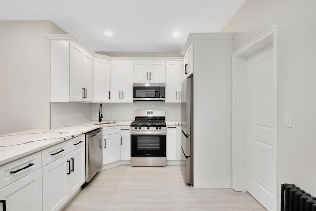 kitchen with sink, white cabinetry, radiator heating unit, stainless steel appliances, and tasteful backsplash