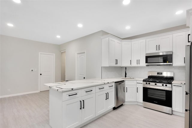 kitchen featuring white cabinetry, tasteful backsplash, light hardwood / wood-style flooring, appliances with stainless steel finishes, and kitchen peninsula