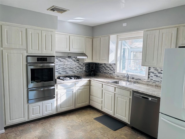 kitchen featuring stainless steel appliances, light stone countertops, sink, and decorative backsplash