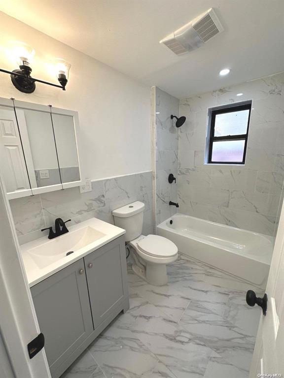 full bathroom with vanity, toilet, tiled shower / bath combo, and tile walls