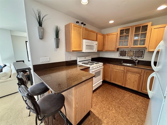 kitchen with sink, a breakfast bar area, kitchen peninsula, white appliances, and dark stone counters