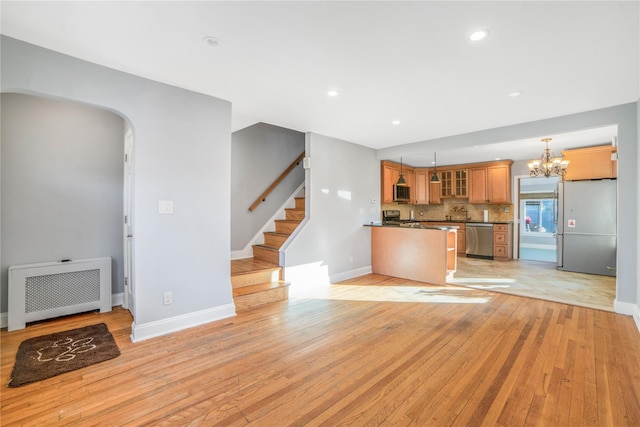 kitchen with appliances with stainless steel finishes, radiator, pendant lighting, decorative backsplash, and light wood-type flooring