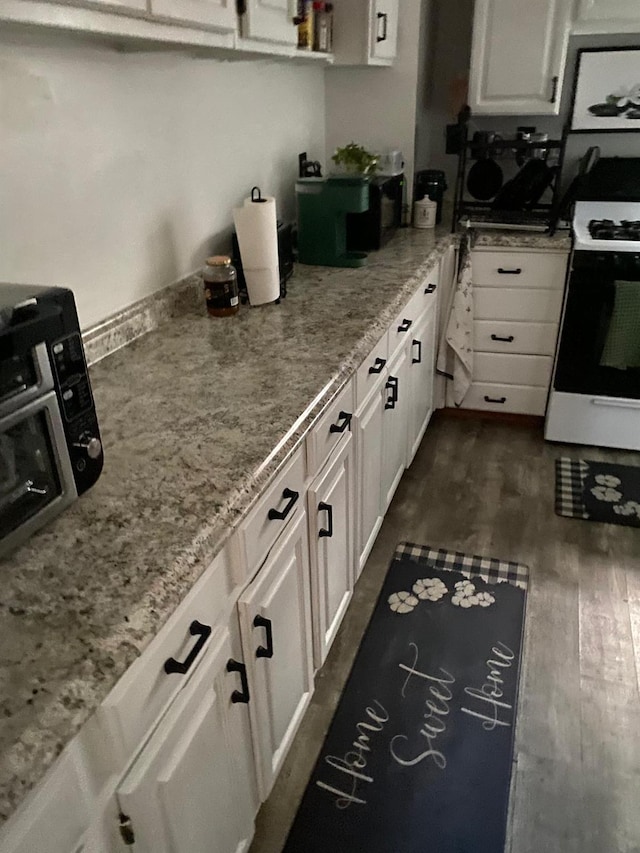 kitchen with light stone counters, dark hardwood / wood-style floors, white cabinets, and range