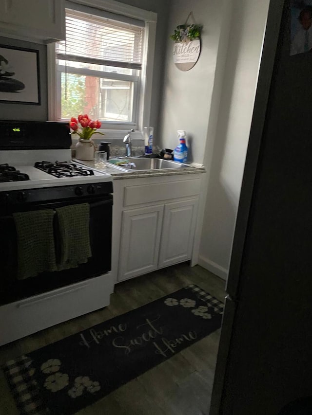 kitchen with sink, black refrigerator, hardwood / wood-style floors, gas range oven, and white cabinets