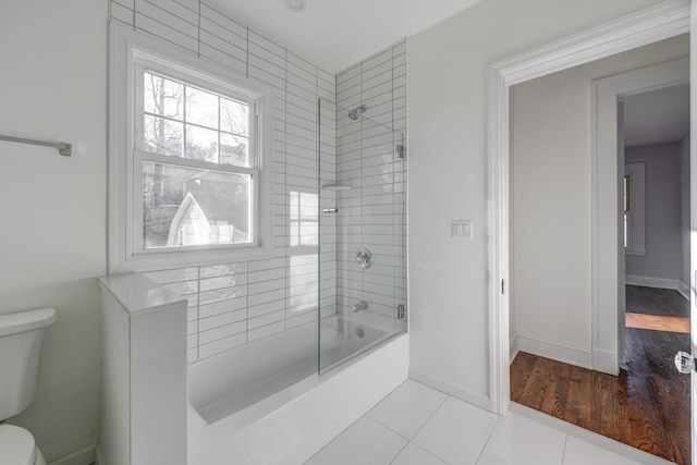 bathroom featuring tile patterned flooring, bath / shower combo with glass door, and toilet