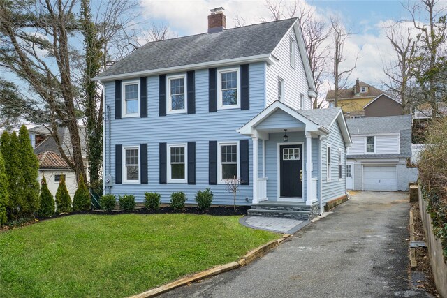 view of front facade featuring driveway, a chimney, roof with shingles, an outdoor structure, and a front yard