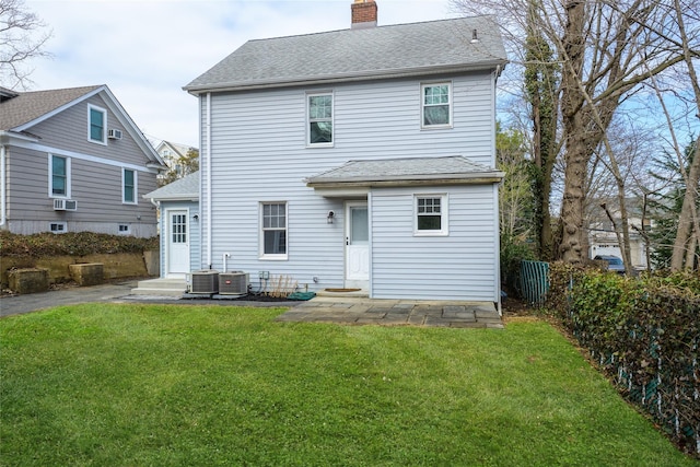 back of house featuring central air condition unit, a chimney, a lawn, and roof with shingles