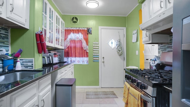 kitchen featuring light tile patterned floors, sink, stainless steel gas range, white cabinetry, and backsplash