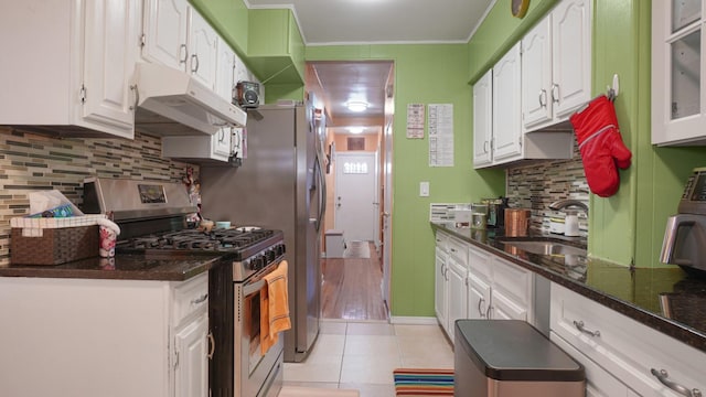 kitchen featuring sink, stainless steel gas stove, white cabinetry, light tile patterned flooring, and dark stone counters