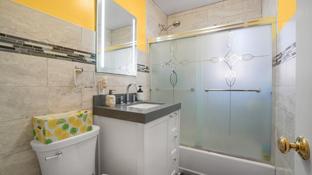 full bathroom featuring bath / shower combo with glass door, tile walls, decorative backsplash, vanity, and toilet