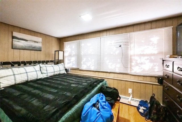 bedroom with multiple windows, a baseboard radiator, hardwood / wood-style floors, and wood walls