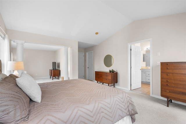 bedroom featuring light colored carpet, vaulted ceiling, decorative columns, and ensuite bathroom