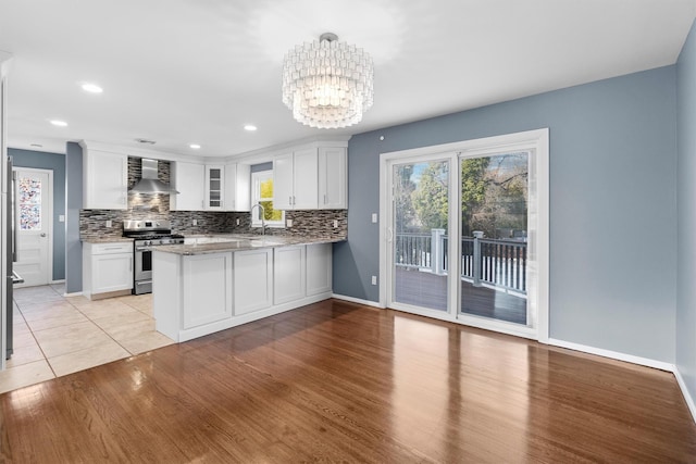 kitchen featuring wall chimney range hood, tasteful backsplash, white cabinets, gas range, and kitchen peninsula