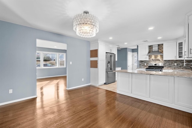 kitchen with wall chimney exhaust hood, white cabinetry, light stone counters, kitchen peninsula, and stainless steel appliances