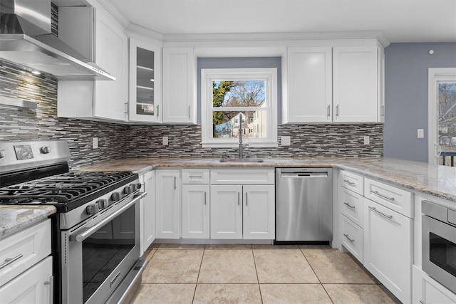 kitchen with light tile patterned floors, stainless steel appliances, light stone counters, white cabinets, and wall chimney exhaust hood