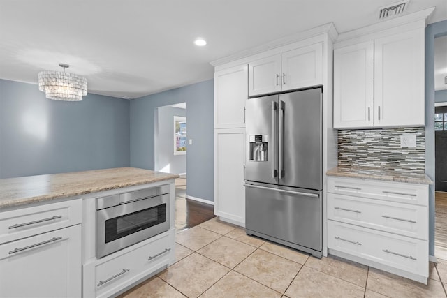 kitchen with light tile patterned floors, white cabinets, pendant lighting, stainless steel appliances, and backsplash