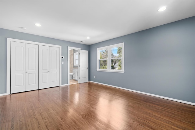 unfurnished bedroom with ensuite bath, hardwood / wood-style floors, and a closet