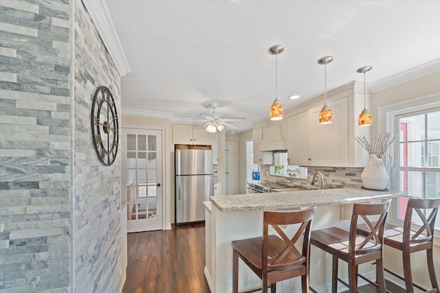 kitchen featuring appliances with stainless steel finishes, dark wood-style flooring, a peninsula, crown molding, and backsplash