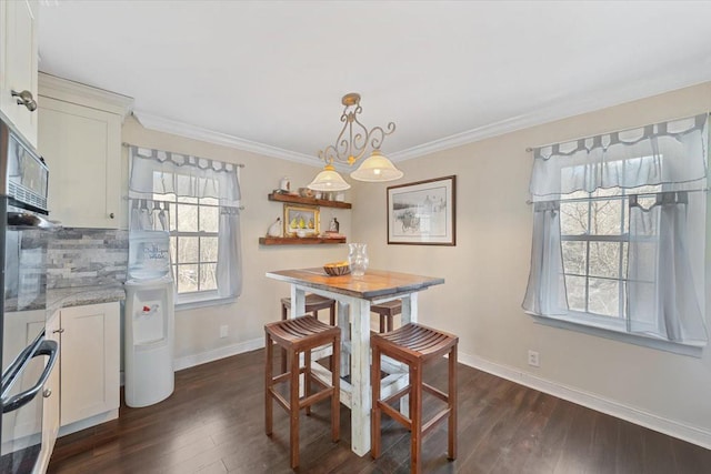 dining space featuring dark wood-type flooring, crown molding, and baseboards