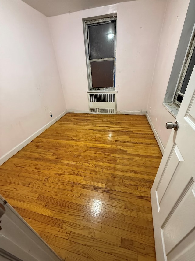 empty room with baseboards, hardwood / wood-style floors, and radiator heating unit