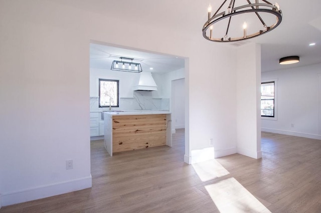 unfurnished dining area with an inviting chandelier, sink, plenty of natural light, and light wood-type flooring