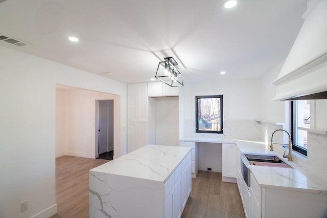 kitchen featuring white cabinetry, premium range hood, a wealth of natural light, and light stone counters