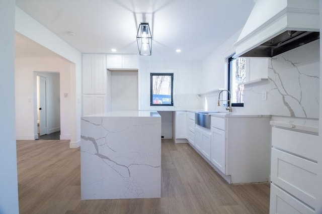 kitchen with light stone countertops, custom range hood, sink, and white cabinets