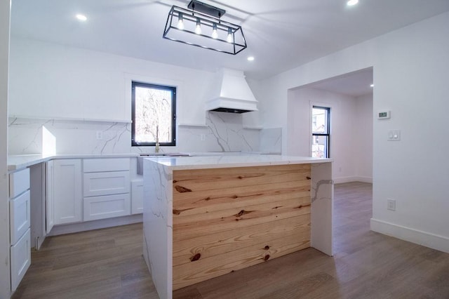 kitchen featuring premium range hood, white cabinetry, light wood-type flooring, and backsplash