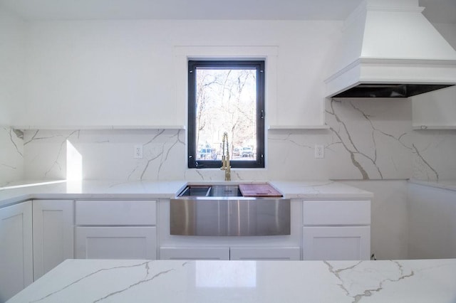 kitchen featuring backsplash, light stone countertops, custom range hood, and white cabinets